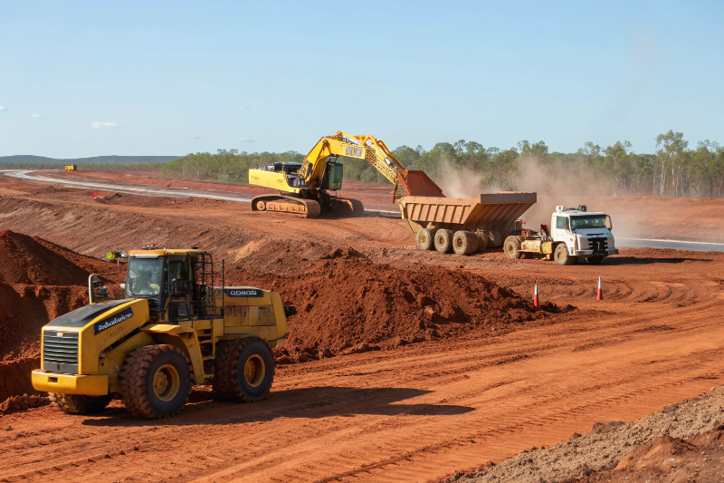 bulk excavation on a vast land Yellow bulldozer pushing soil in foreground, large excavator loading an articulated dump truck in middle ground, and water cart spraying for dust suppression in background.